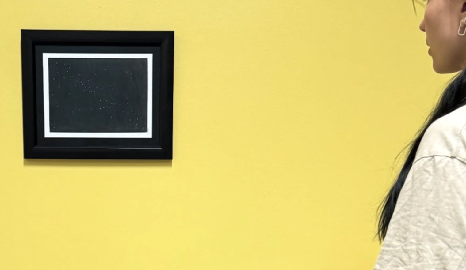 A framed star-field artwork installed on a gallery wall, viewed by a passerby